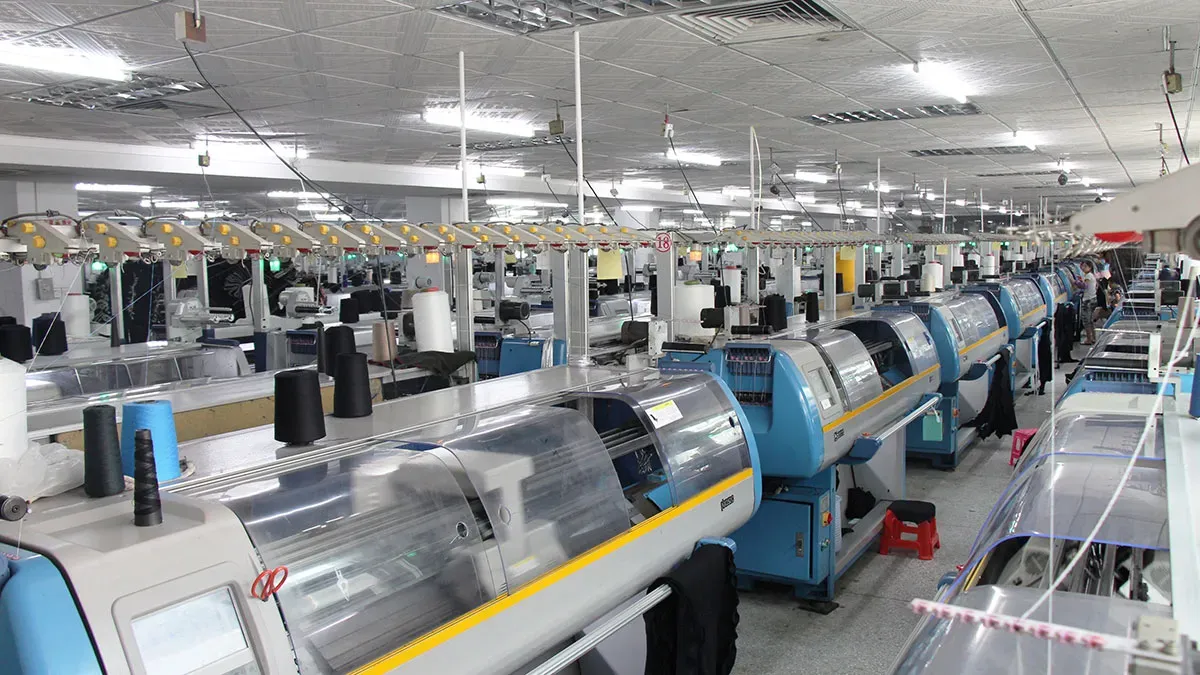 Large-scale knitwear manufacturing facility featuring rows of advanced automated computerized flat knitting machines at JM Sweater.