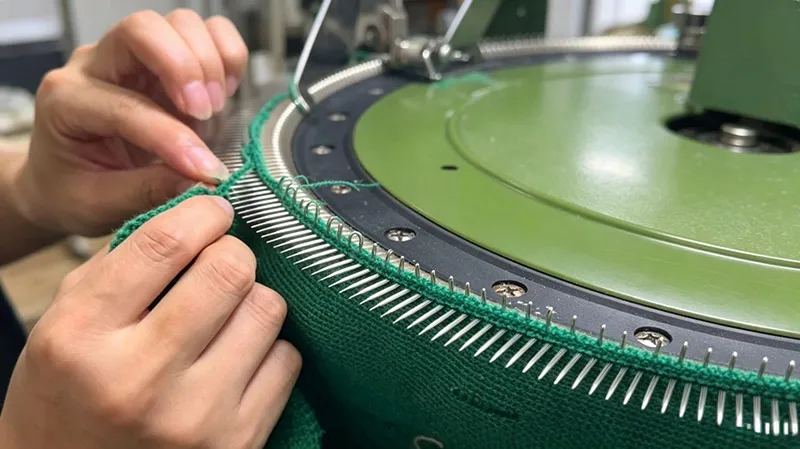 Master craftsperson performing loop-by-loop hand-linking on a sweater collar in a professional garment factory