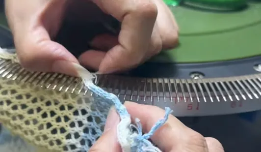 Skilled factory technician performing precision hand-linking seam assembly on a circular looping machine
